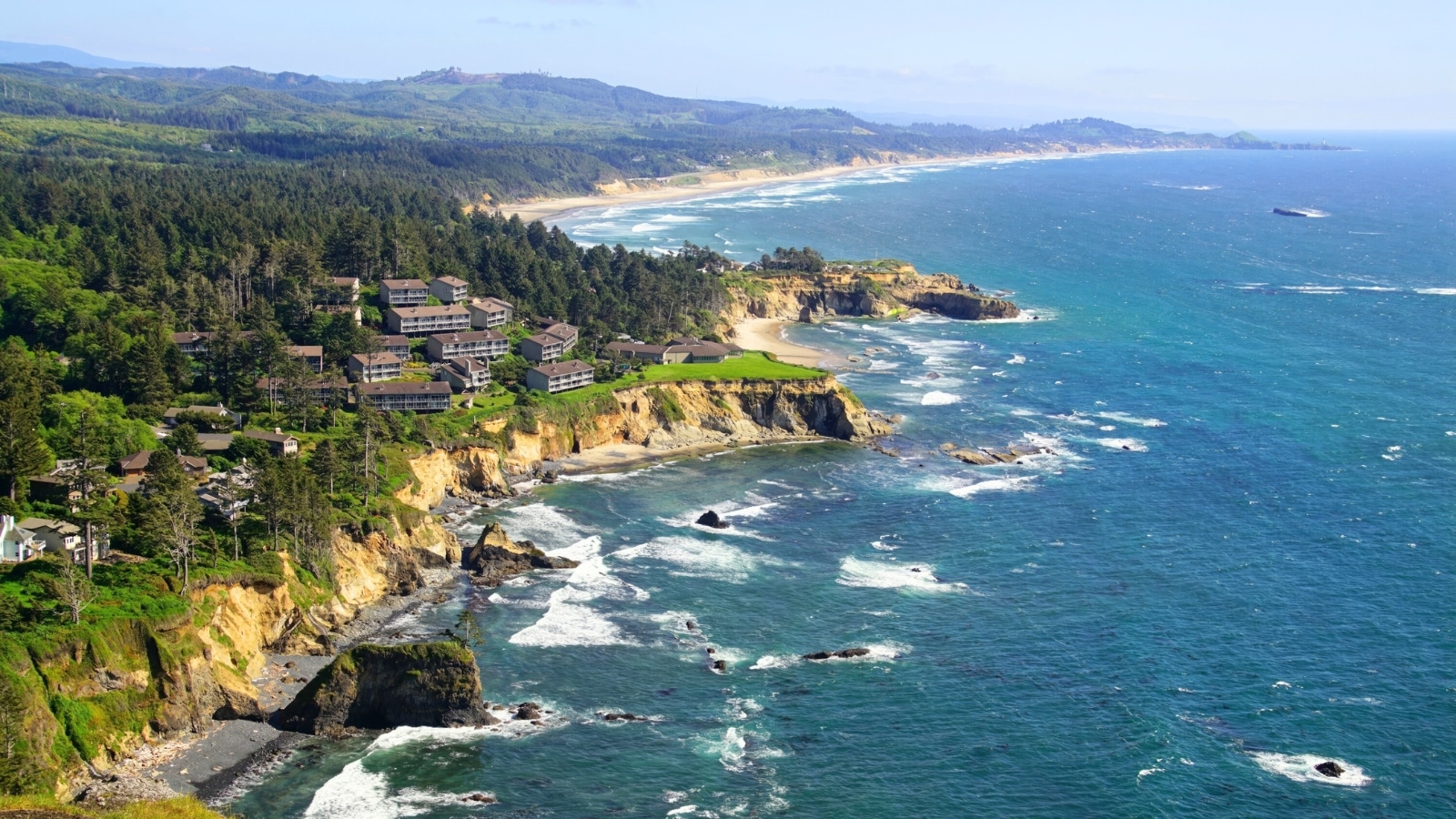 Condominiums nestled amidst a conifer forest, extending across headlands near Otter Rock, close to Depoe Bay, Oregon. The buildings blend harmoniously with the natural surroundings, showcasing a mix of residential and vacation properties.