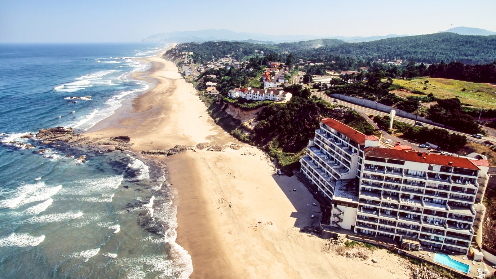 Lincoln City and its surroundings in Oregon, USA. The beach is depicted as long and wide, stretching alongside the ocean with small waves visible. On the right side of the beach, there are several hotel complexes.