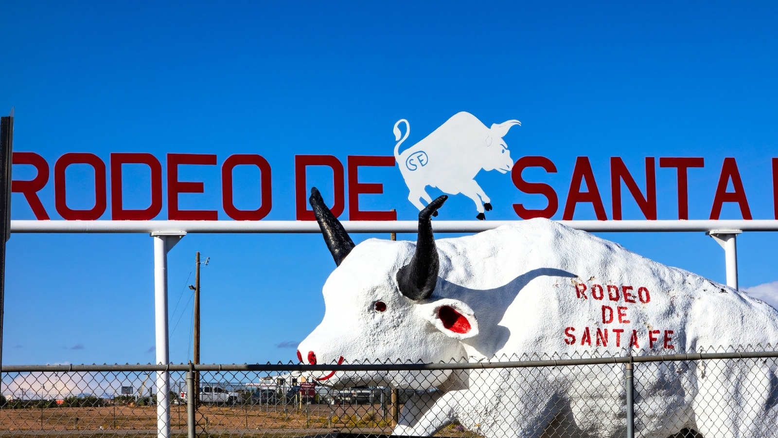In Santa Fe, New Mexico, a close-up of a red sign reads "Rodeo De Santa Fe," drawing attention to the event. Below the sign, a sculpture of a white bull is prominently displayed.