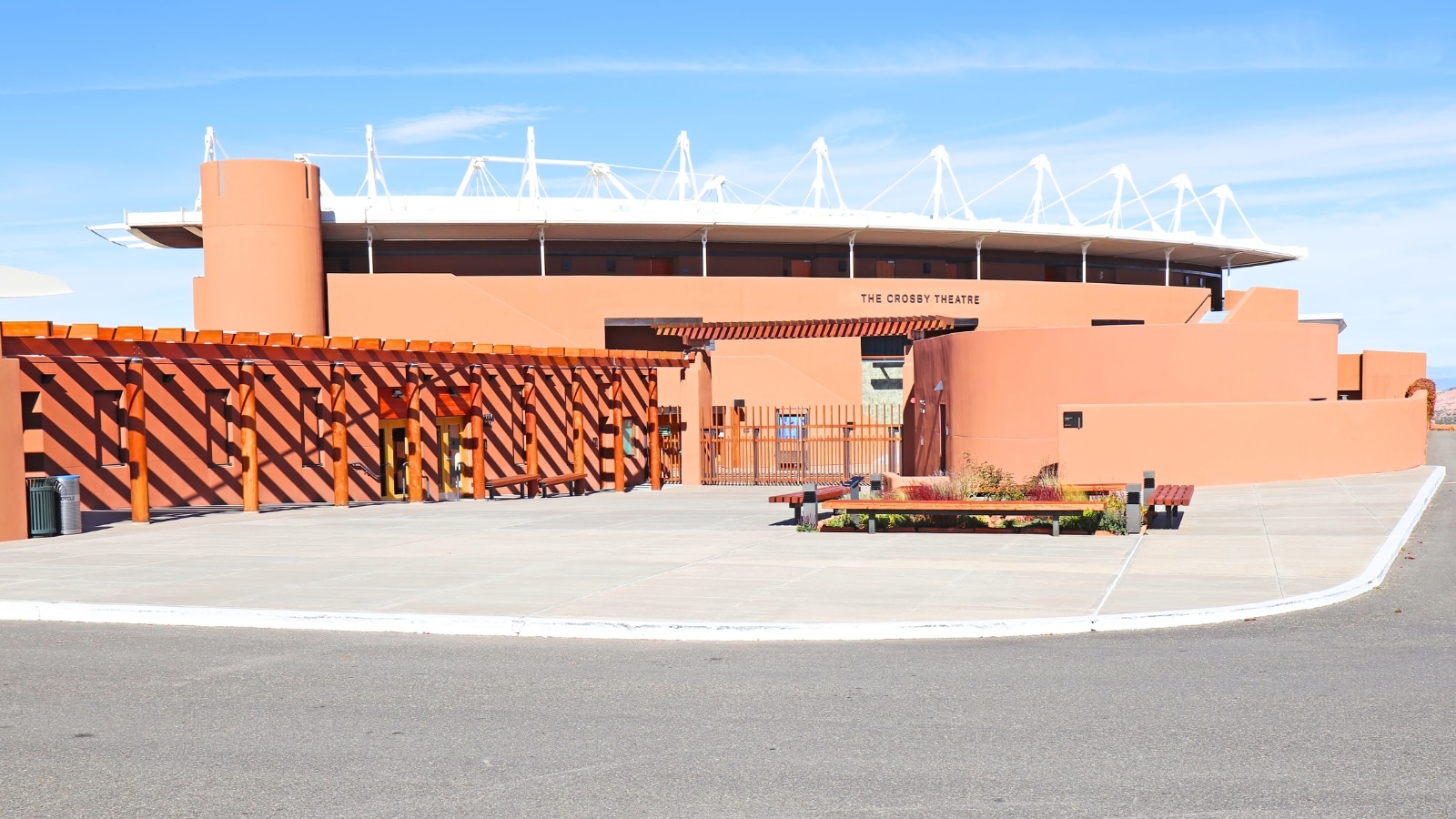 The external facade of the Crosby Theatre at the Santa Fe Opera (SFO). The color scheme of the facade is a mix of warm earth tones, reflecting the desert landscape of Santa Fe.