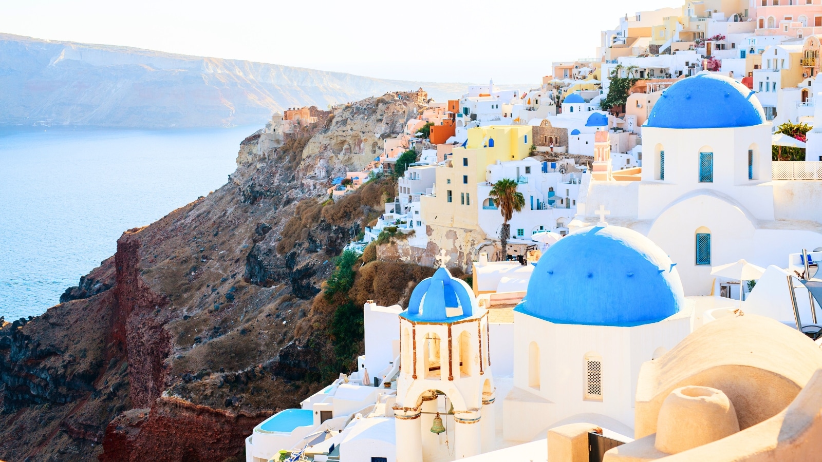 A blue-domed church in Oia overlooks the spectacular caldera surrounding Santorini Island in Greece. The church's architecture features traditional Cycladic style with whitewashed walls and striking blue domes. Surrounding the church is the breathtaking view of the caldera, characterized by rugged cliffs and deep blue waters.