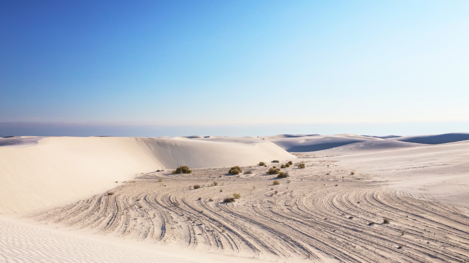 White Sands National Monument in New Mexico, USA, known for its distinctive white gypsum sand dunes. The desert terrain creates a surreal and otherworldly atmosphere. The white dunes stretch across the landscape, creating a stark contrast against the clear blue sky.