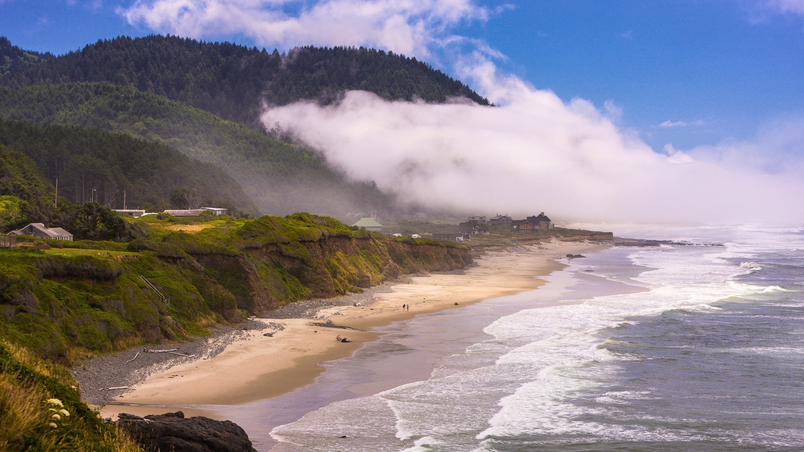 Yachats, Oregon, USA, capturing the surf and beach along the central Oregon coast from Brays Point. The beach appears wide with small ocean waves gently rolling in. On the left side of the image, there is a coast lined with hills abundant in vegetation.
