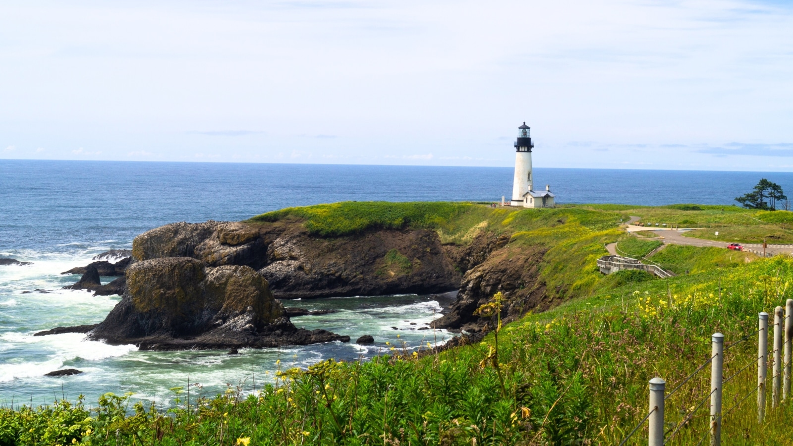 Yaquina Head Lighthouse, situated in Newport, Oregon, USA, within the Yaquina Head Outstanding Natural Area. The lighthouse stands tall against the coastal backdrop, its classic white structure contrasting with the deep blue of the ocean and the clear sky above.