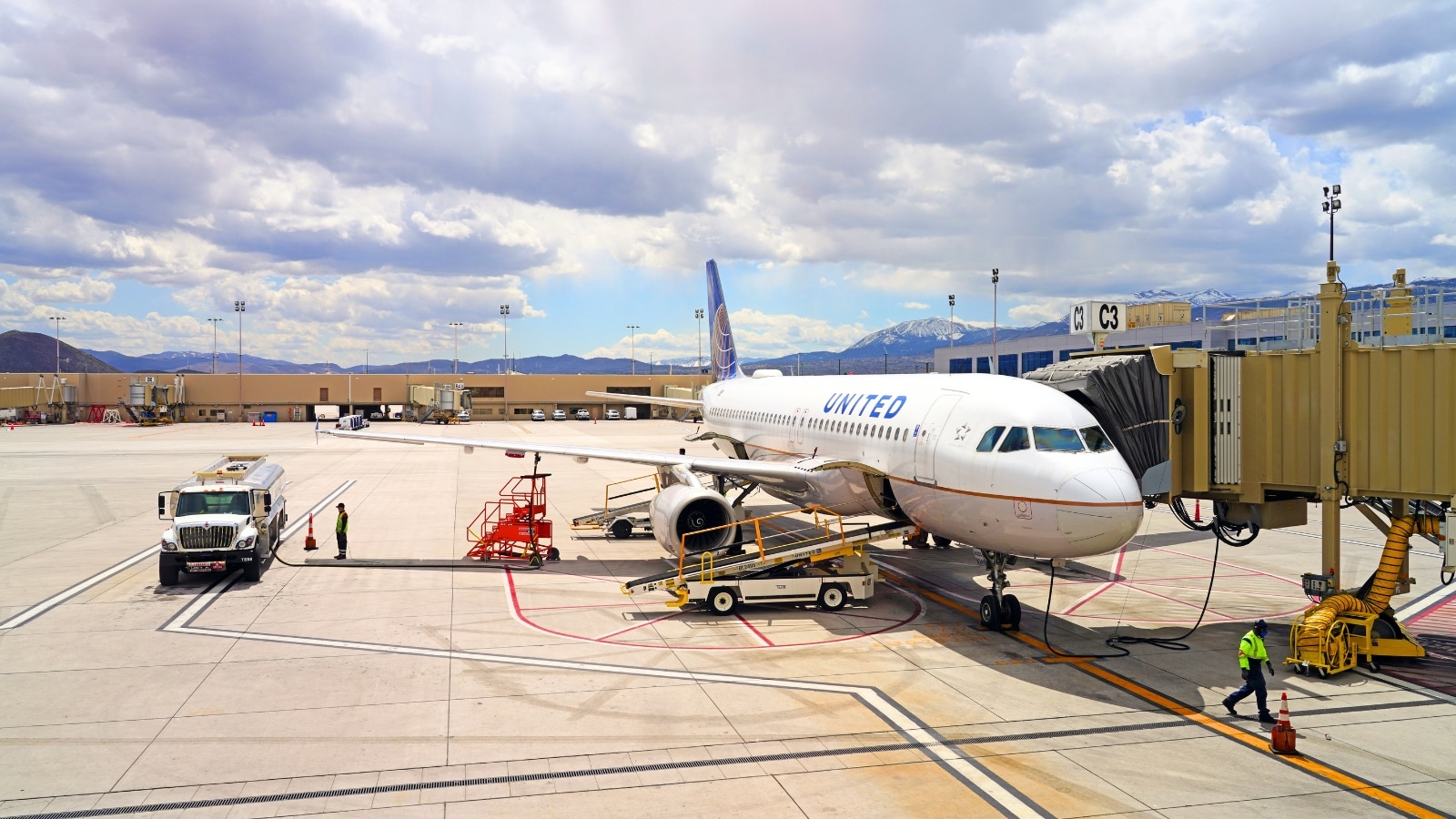 United Airlines airplane at Reno-Tahoe International Airport in Reno, NV. The plane is predominantly white with prominent United lettering and a blue tail, typical of the airline's branding. The sky appears overcast with clouds.