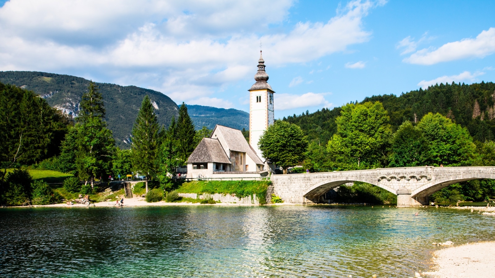 The Church of St. John the Baptist stands near Bohinj Lake in Slovenia. This charming church features a traditional design with a sloped roof and a bell tower. Surrounding the church are lush green trees and the serene waters of Bohinj Lake.