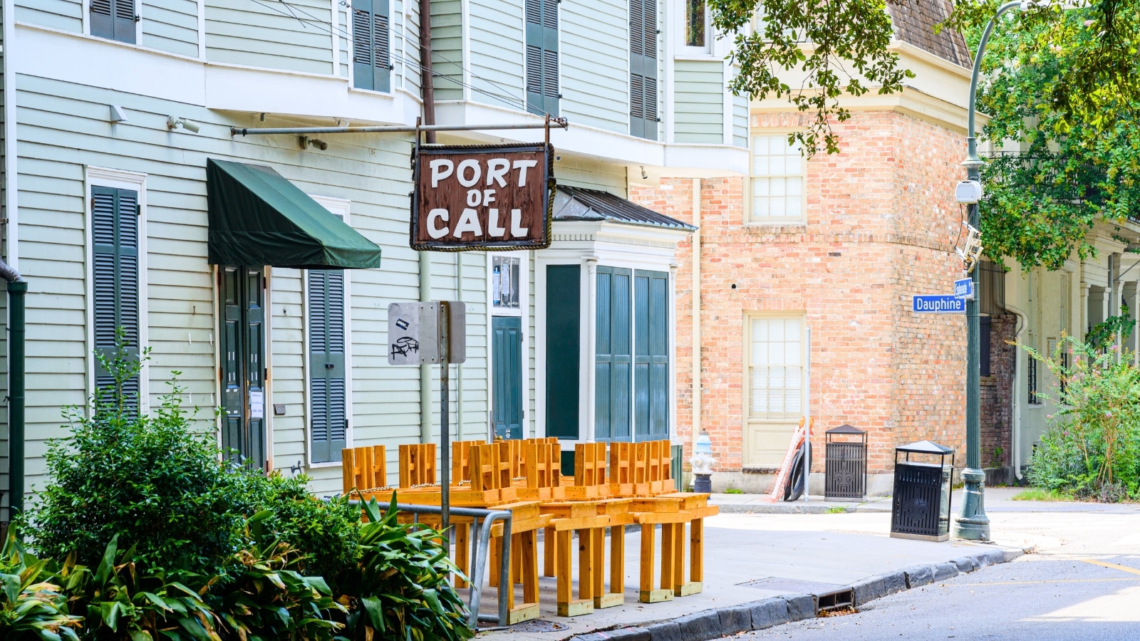 Port of Call Restaurant on Esplanade Avenue in New Orleans, LA, features wooden tables and chairs at the entrance. A brown-colored sign with the inscription "Port of Call" is prominently displayed. The restaurant's exterior combines rustic elements with a welcoming ambiance.