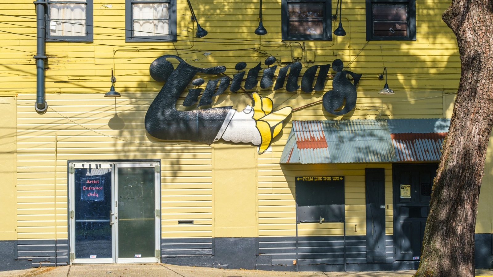 The side entrance of Tipitina's music club in Uptown New Orleans features a yellow building with a black logo sign. The building's exterior is vibrant and eye-catching, reflecting the lively music scene of the city. The black logo stands out against the yellow background.