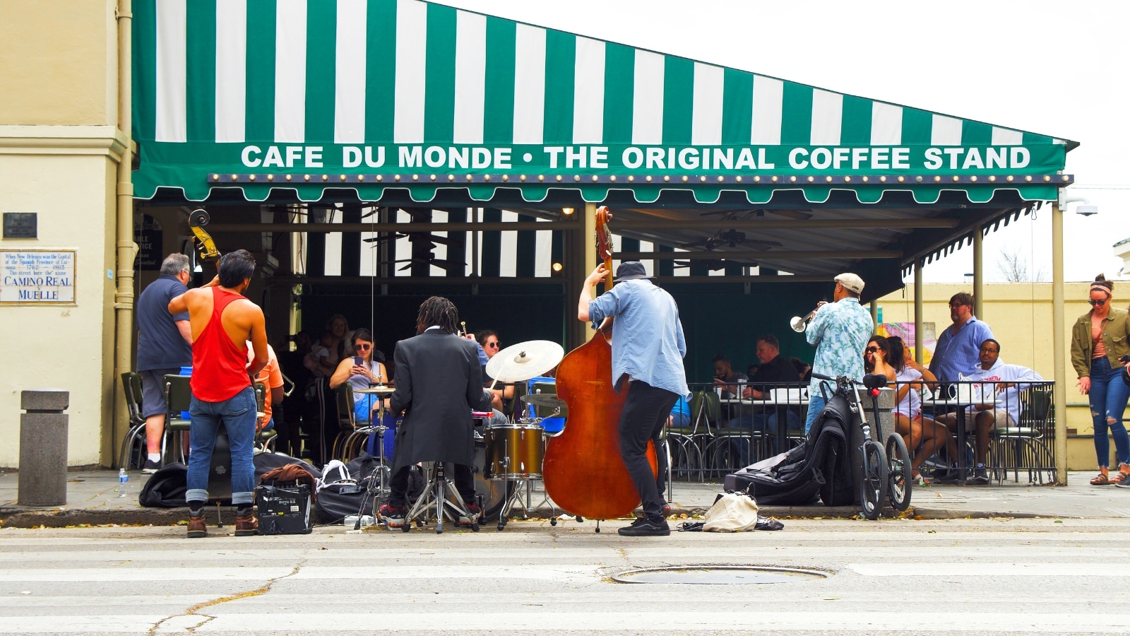 In New Orleans, musicians perform outside the renowned Cafe Du Monde. The green tent with the cafe's name is clearly visible.