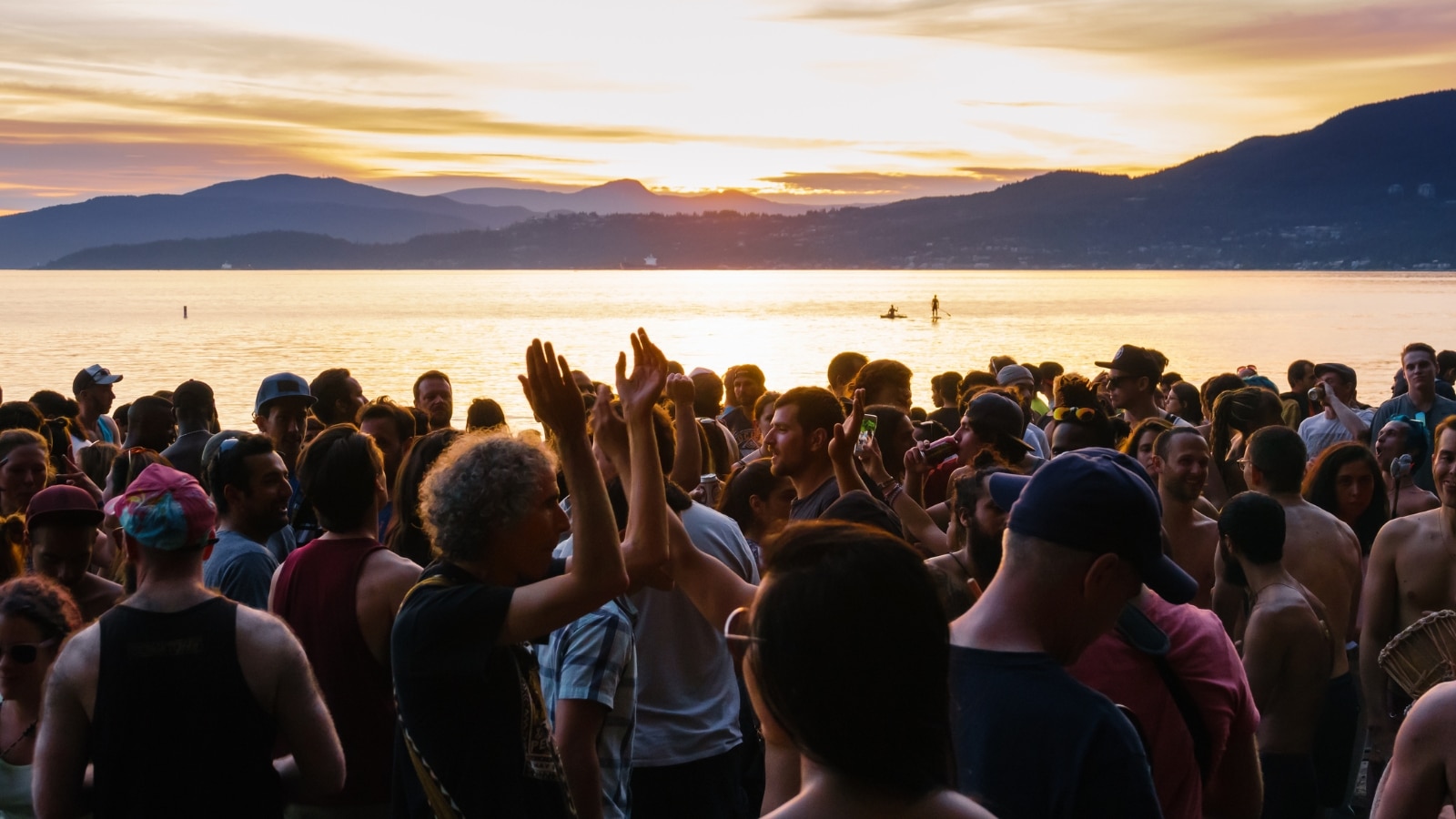 The image depicts a lively scene at Lake Tahoe, where a crowd of people is gathered outdoors on the beach, engaging in dancing and listening to live music. In the background, hills can be seen.