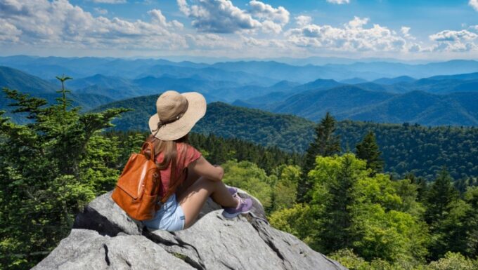 Hiker girl sitting on a cliff edge enjoying scenic summer view. Woman relaxing on top of autumn mountain, over the clouds. Blue Ridge Parkway ,near Asheville, North Carolina, USA.