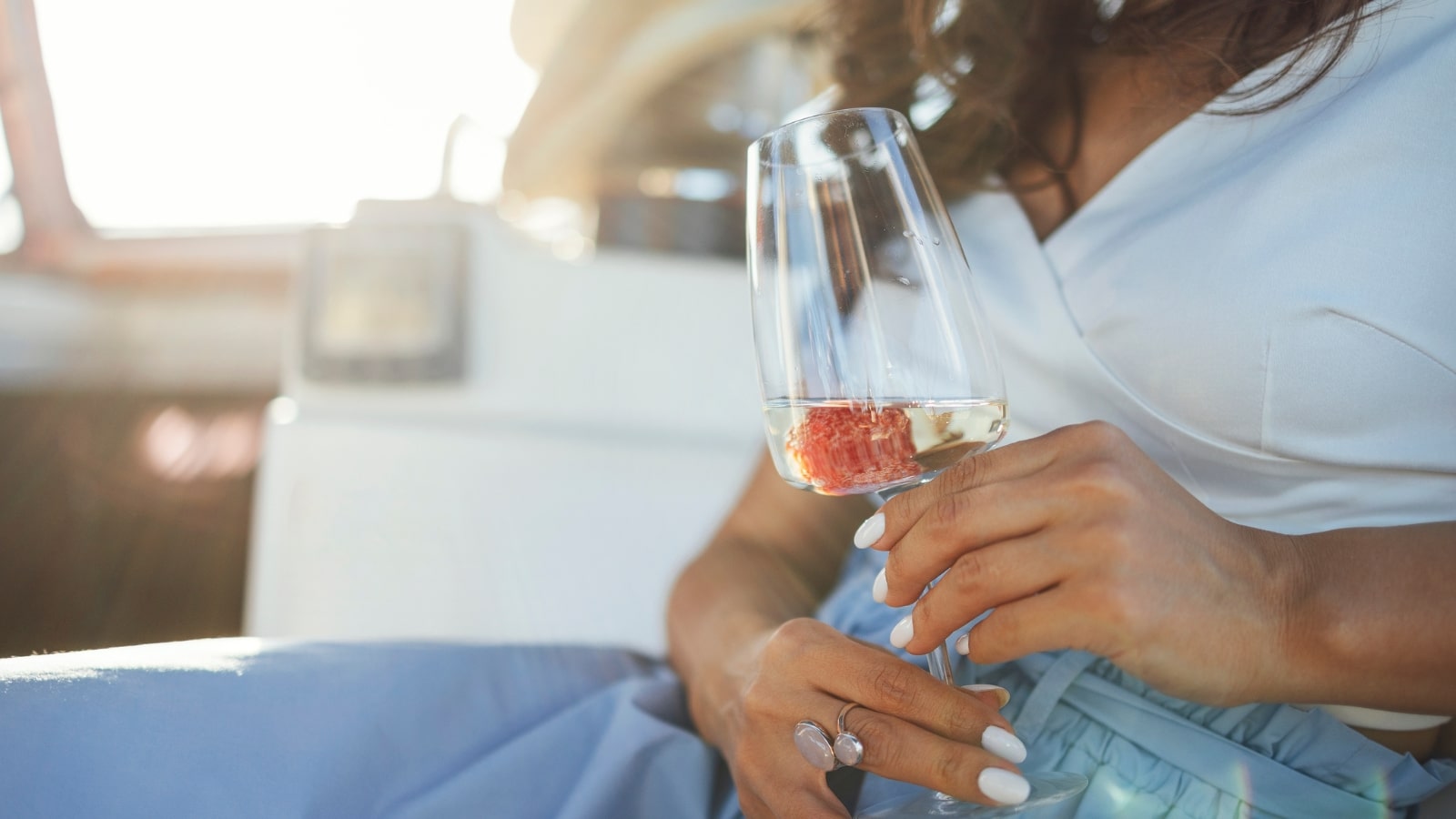 The image features a close-up of a woman's hand holding a glass of wine aboard a boat.