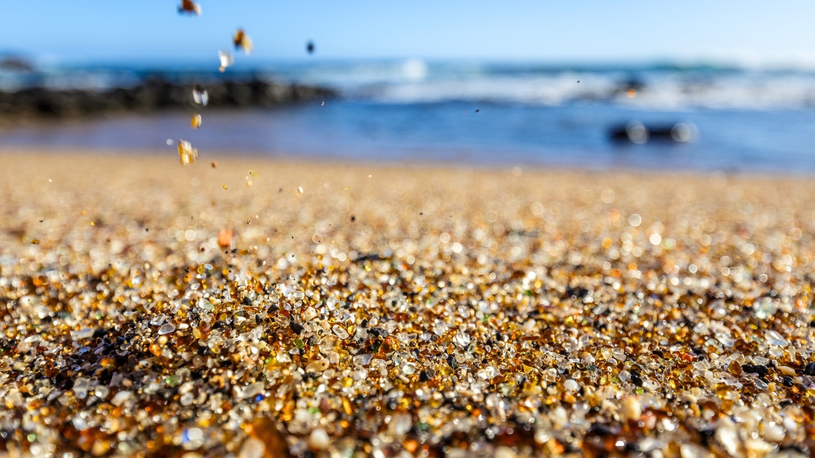 Small polished glass fragments cover Glass Beach on the south coast of Kauai, Hawaii. The beach consists of vibrant pieces of glass in various colors such as green, blue, brown, and clear. These fragments glisten under the sunlight, creating a unique and picturesque setting.
