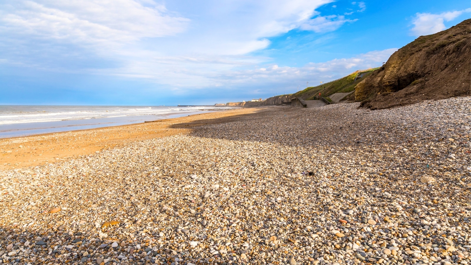 Seaham Beach in England features a rugged coastline with pebbled shores and rocky outcrops. The beach consists of smooth, multicolored stones and stretches of sand.