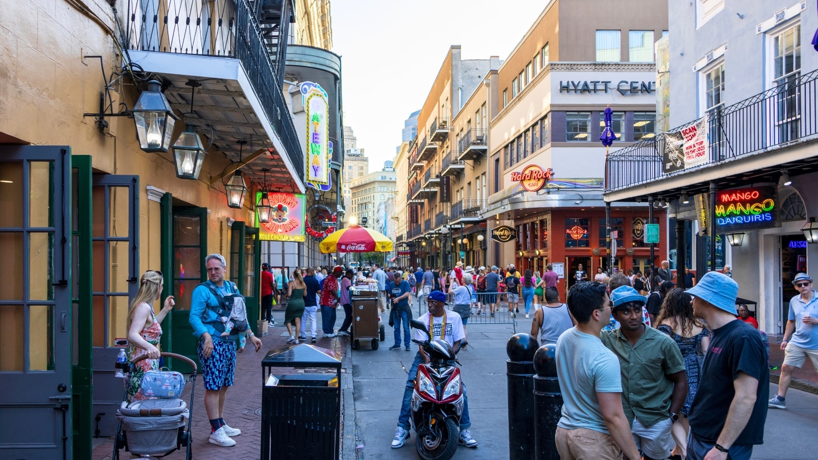Bourbon Street in the French Quarter of New Orleans, Louisiana, features a lively atmosphere with people walking along the street. The area is lined with restaurants and bars, their colorful signs and vibrant facades. 