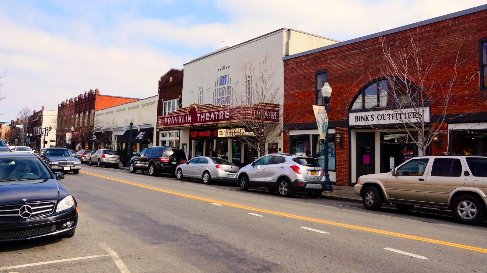 Main Street in Franklin, Tennessee showcases classic brick buildings, the famous Franklin Theater, various shops and restaurants, and various parked cars along the sidewalks.